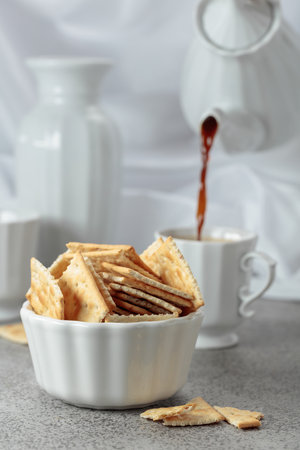 Crunchy square crackers and black coffee. In the background, black coffee is being poured from a coffee pot into a cup.の写真素材