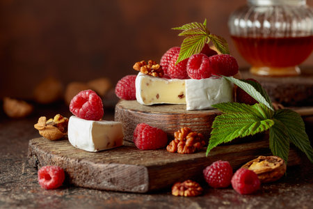 Camembert cheese with fresh raspberries and walnuts on a brown vintage table.