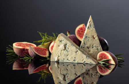 Blue cheese with fresh figs and rosemary on a black reflective background.の写真素材