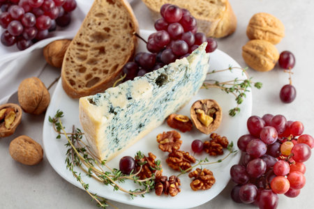 Gorgonzola cheese with walnuts, red grapes, and thyme on a white kitchen table.の写真素材