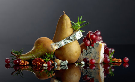 Blue cheese with pear, walnuts, red grapes, and rosemary. Tradition blue mold cheese with fruits on a black reflective background. Copy space.の写真素材