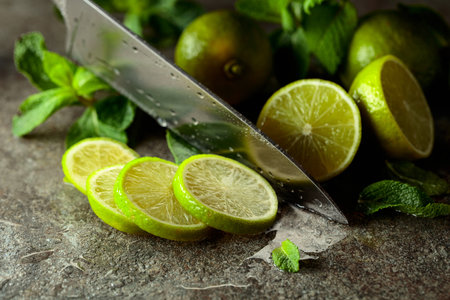 A knife, slices of lime and sprigs of fresh mint on a wet stone table.の写真素材