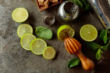 Wooden citrus squeezer, shaker, and ingredients for making summer refreshing drinks. Brown sugar, limes, and fresh mint branches on a stone table.の写真素材