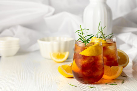 Iced tea or alcoholic cocktail with ice, rosemary and lemon slices on the white table. Fresh healthy cold lemon beverage. Tea with ice and lemon.の写真素材