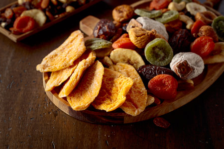 Dried mango slices, tropical fruits, nuts, and raisins on an old wooden table.の写真素材