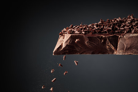 Large piece of dark chocolate and falling chocolate crumbs on a black background.の写真素材