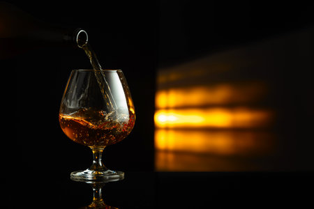 Pouring brandy from a bottle into a snifter on a black reflective background. Copy space.の写真素材