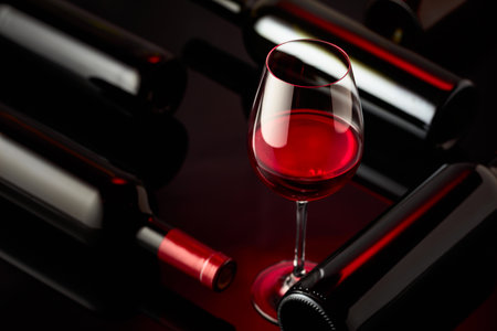 Glass and bottles of red wine on a black reflective background. Selective focus.の写真素材