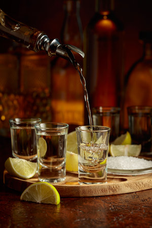 Gold tequila with salt and lime slices on a brown background. Tequila is poured into a glass.の写真素材