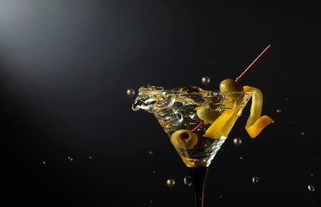 Glass of classic dry martini cocktail with green olives on a black background. Martini with splashes. Free space for your text.の写真素材
