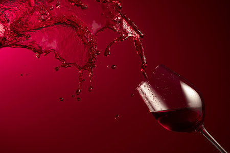Glass and red wine splash on a dark red background. Copy space.の写真素材
