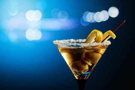 Glass of Martini with green olives and lemon peel on a blue background. Copy space.の写真素材