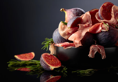 Prosciutto with rosemary and fig fruit in black dish on a black reflective background. Traditional Italian snack.の写真素材