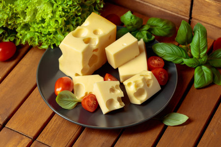 Swiss cheese, green basil, salad, and tomatoes on a natural brown wooden background. Soft, diffused light.の写真素材