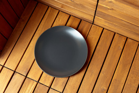 Empty black plate on natural wooden background. Soft, diffused light from top left. Place your product on the plate. Copy space.の写真素材