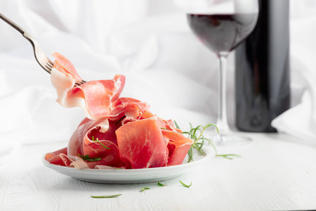 Prosciutto with rosemary and red wine on a white wooden table. Traditional Italian snack.の写真素材