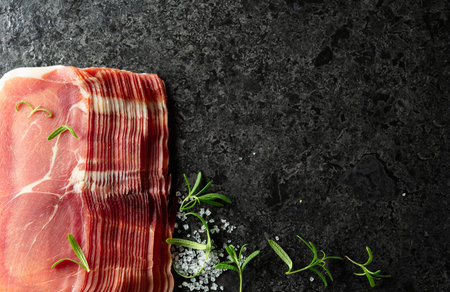 Sliced prosciutto and rosemary on a stone table. Top view.の写真素材