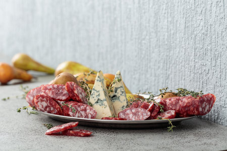 Blue cheese, dry-cured sausages, thyme and pears on a gray stone table.の写真素材