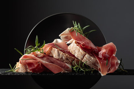 Ciabatta with prosciutto and rosemary on a black background. Traditional Italian snack.の写真素材