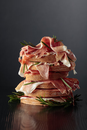 Italian prosciutto or Spanish jamon with bread and rosemary on a black wooden table. Copy space.の写真素材