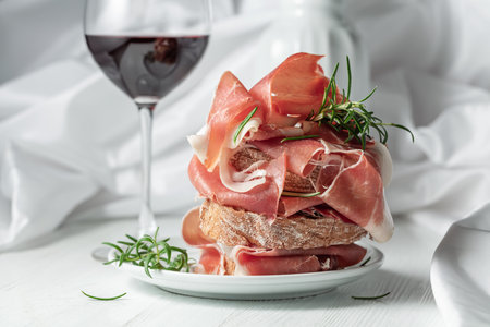 Ciabatta with prosciutto, rosemary and glass of red wine on a white wooden table. Traditional Italian snack.の写真素材