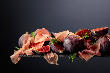 Prosciutto with rosemary and fig fruit on a black background. Traditional Italian snack. Copy space.の写真素材