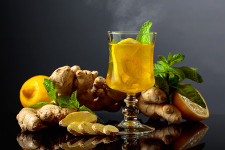 Ginger tea with lemon and mint on a black reflective background.