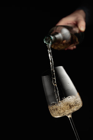 Pouring white wine in a glass goblet. Black background with copy space.の写真素材