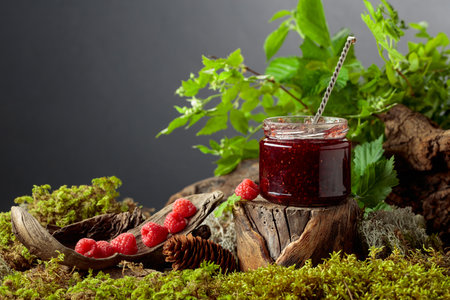 A jar of raspberry jam with fresh berries on an old tree trunk in the forest. A concept of healthy,...