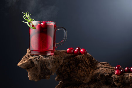 Hot drink with cranberries, lime, and rosemary on an old wooden snag. Black background with copy space.の写真素材
