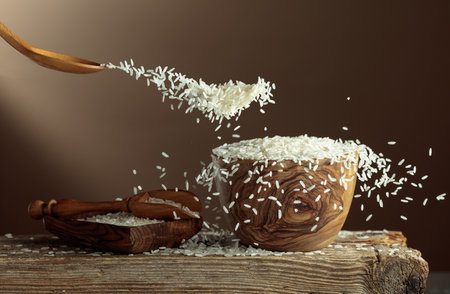 Stop-motion white rice splash on a beige background. Rice is poured into a wooden bowl. Copy space.の写真素材