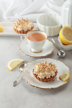 Meringue lemon tart. Meringue tart, cup of tea, lemon slices, and white kitchen utensils on a white marble countertop.の写真素材
