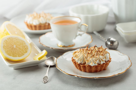 Meringue lemon tart. Meringue tart, cup of tea, lemon slices, and white kitchen utensils on a white marble countertop.の写真素材