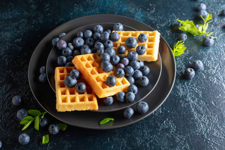 Belgian waffles with blueberries on a dark blue table.の写真素材