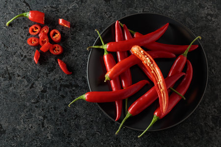 Fresh red chili peppers with green stems on a black stone table. Top view, copy space.