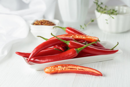 Fresh red chili peppers with green stems on a white wooden table.の写真素材