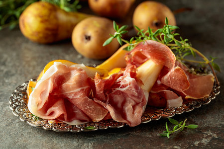Prosciutto with pears and thyme on a silver tray. Traditional Mediterranean snack on a stone table.の写真素材