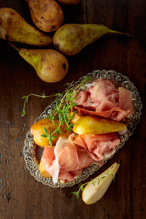 Prosciutto with pears and thyme on a silver tray. Traditional Mediterranean snack with red wine. Top view.の写真素材