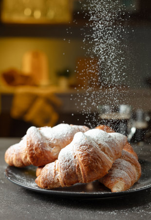 Fresh baked croissants and black coffee on a kitchen table. Croissants sprinkled with sugar powder. Selective focus.の写真素材
