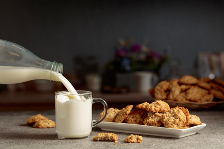 Oatmeal cookies and milk on a kitchen table. Milk is poured from a bottle into a glass mug. Copy space.の写真素材