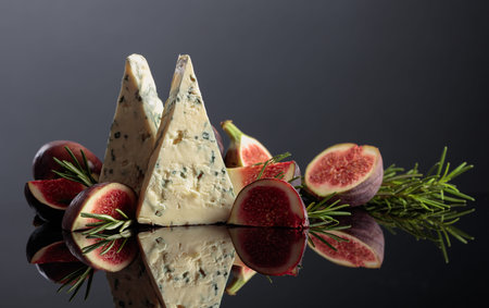 Blue cheese with fresh figs and rosemary on a black reflective background.