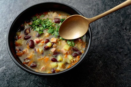 Red bean soup with potatoes, tomatoes, carrots, and bacon on a black stone table. Top view. Copy...