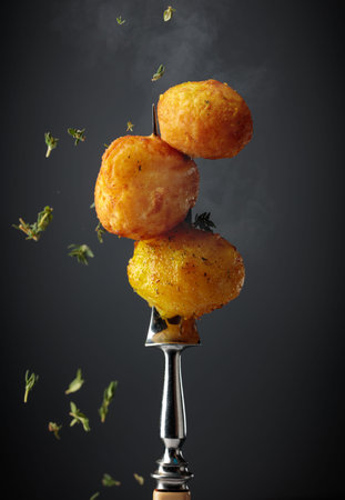Roasted potatoes on a fork, sprinkled with a fresh thyme. Black background.