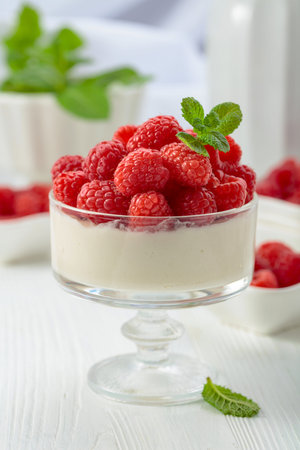 Panna cotta with fresh raspberries in a clear bowl on a white wooden table. Berry parfait delight...