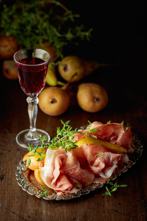 Prosciutto with pears and thyme on a silver tray. Traditional Mediterranean snack with red wine.の写真素材