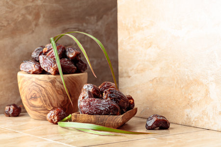 Fresh dates fruit in a wooden dish on a beige ceramic table.