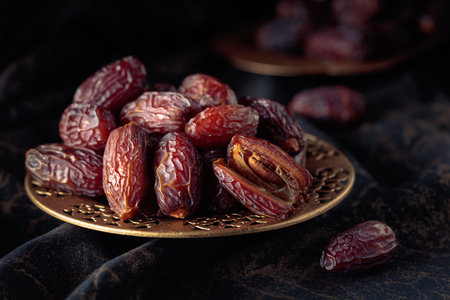 Dates fruits in a golden bowl on black fabric with gold ornamentation. Traditional Arab healthy...