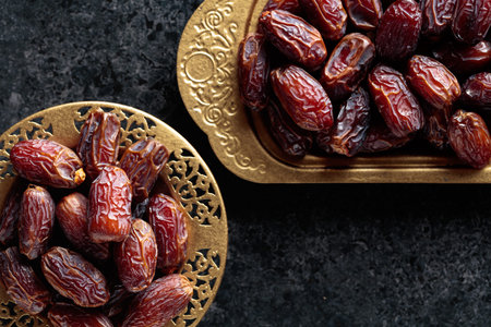 Dates fruits in a golden bowls on black stone table. Traditional Arab healthy food. Top view. Copy...