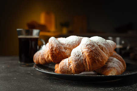 Fresh baked croissants and black coffee on a kitchen table. Croissants sprinkled with sugar powder. Selective focus.の写真素材