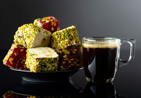 Turkish delights with pistachio and black coffee on a black reflective background.